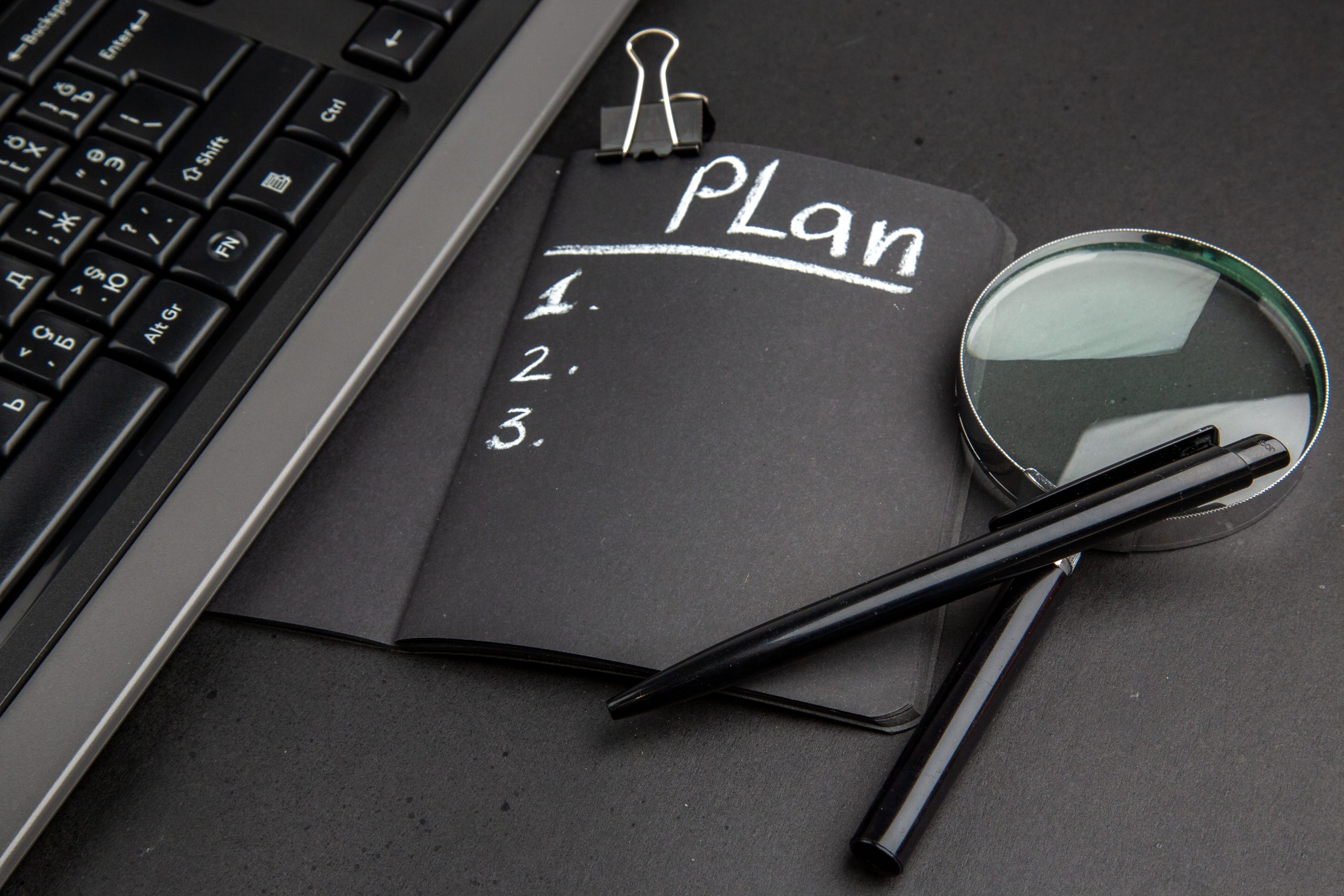 A notebook with the word "plan" and a magnifier on a black background